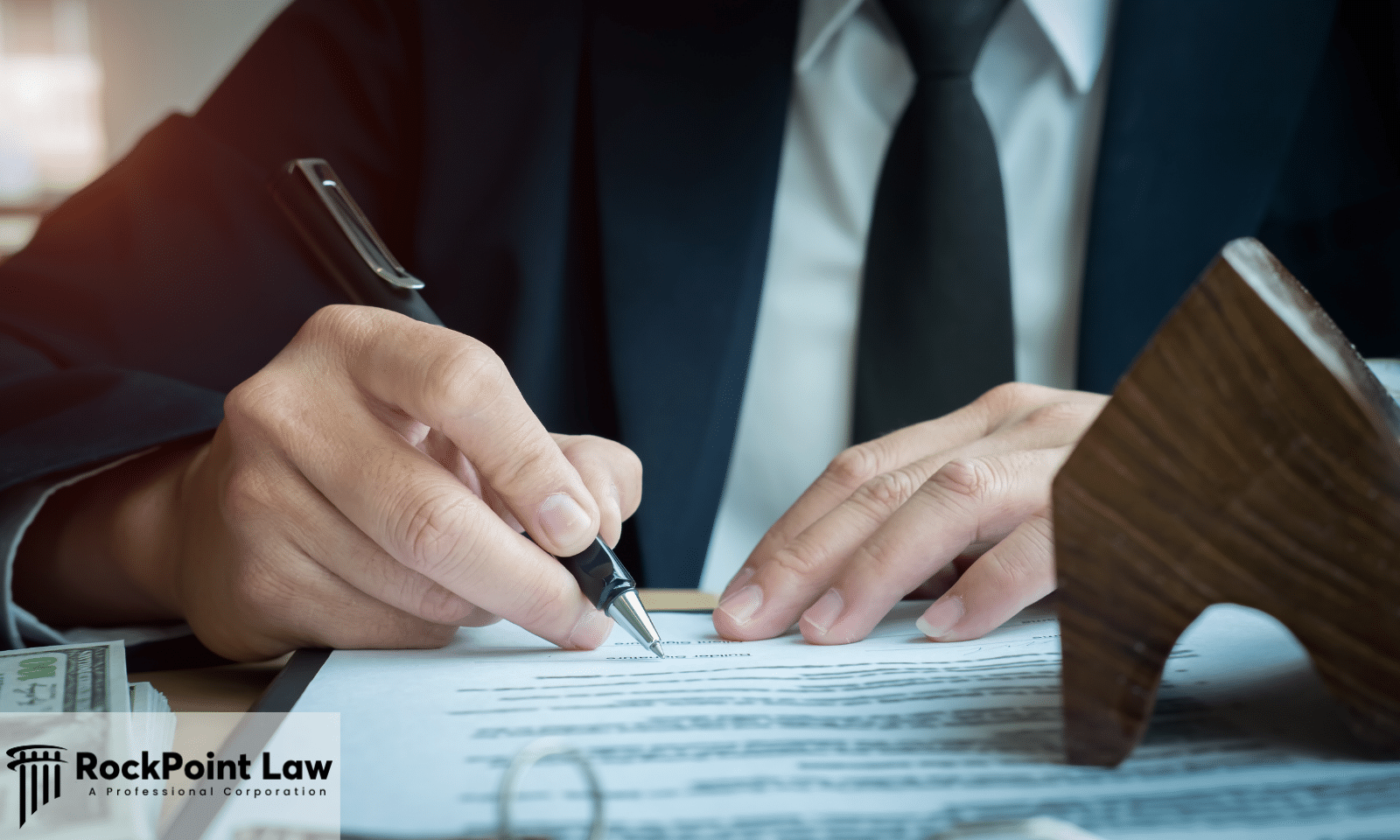 Close-up of an attorney signing a legal document at a desk with a pen, contract paperwork, and legal office accessories.
