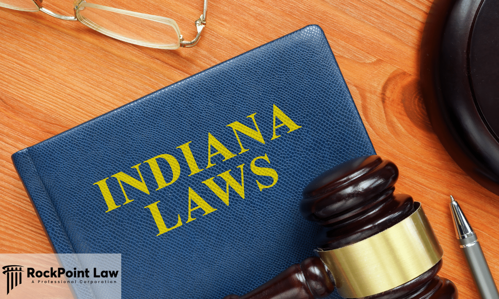 Judge's gavel resting on a law book labeled "Indiana Laws" with a pen and eyeglasses on a wooden desk.