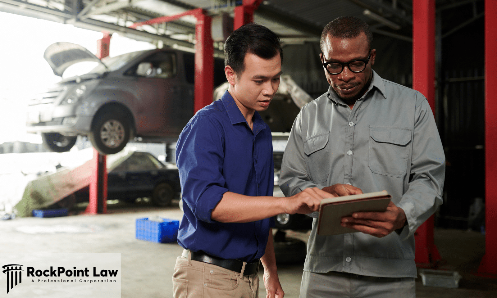 Vehicle owner and service advisor reviewing repair records on a tablet at an automotive repair shop.