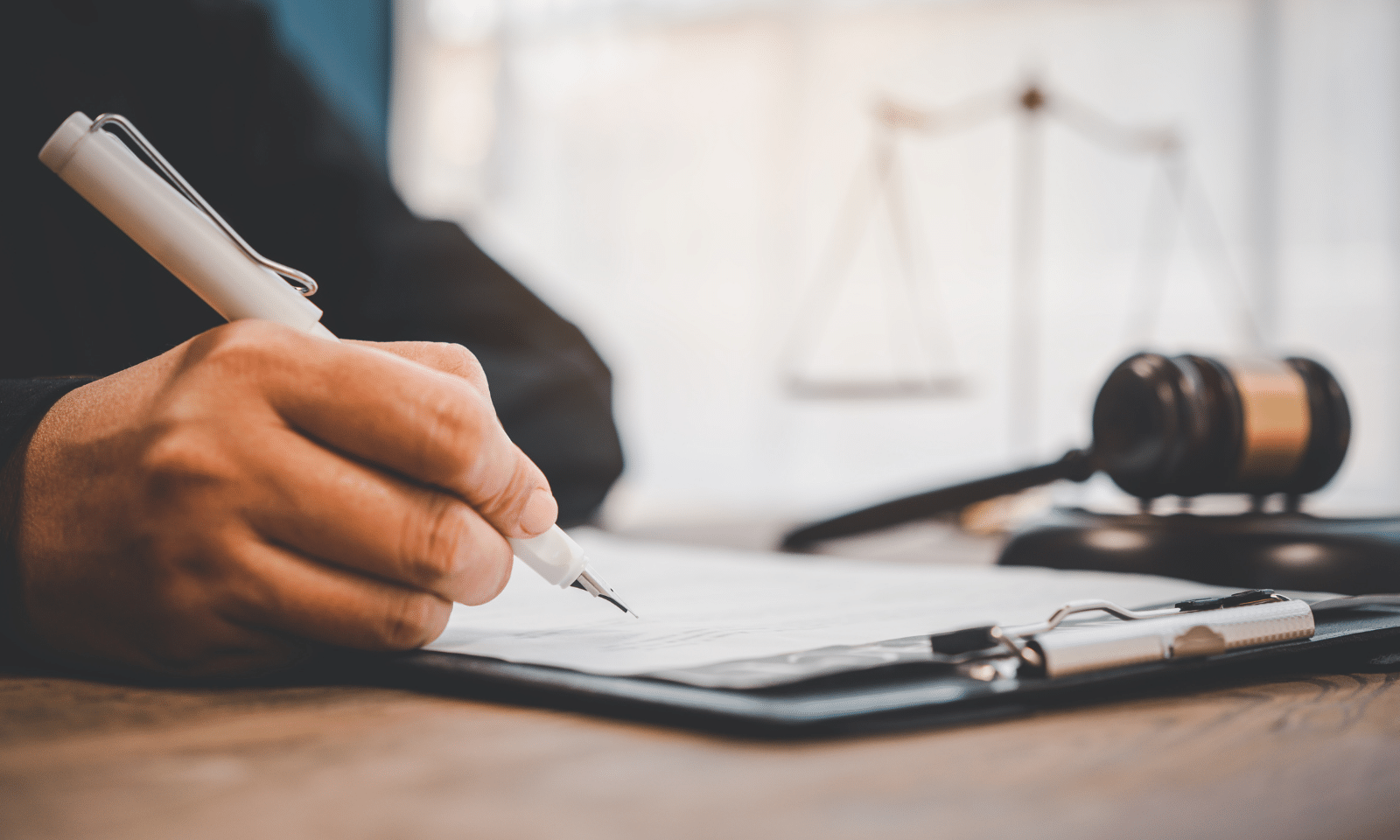 Close-up of a person signing Lemon Law claim documents on a clipboard with a judge's gavel and scales of justice.