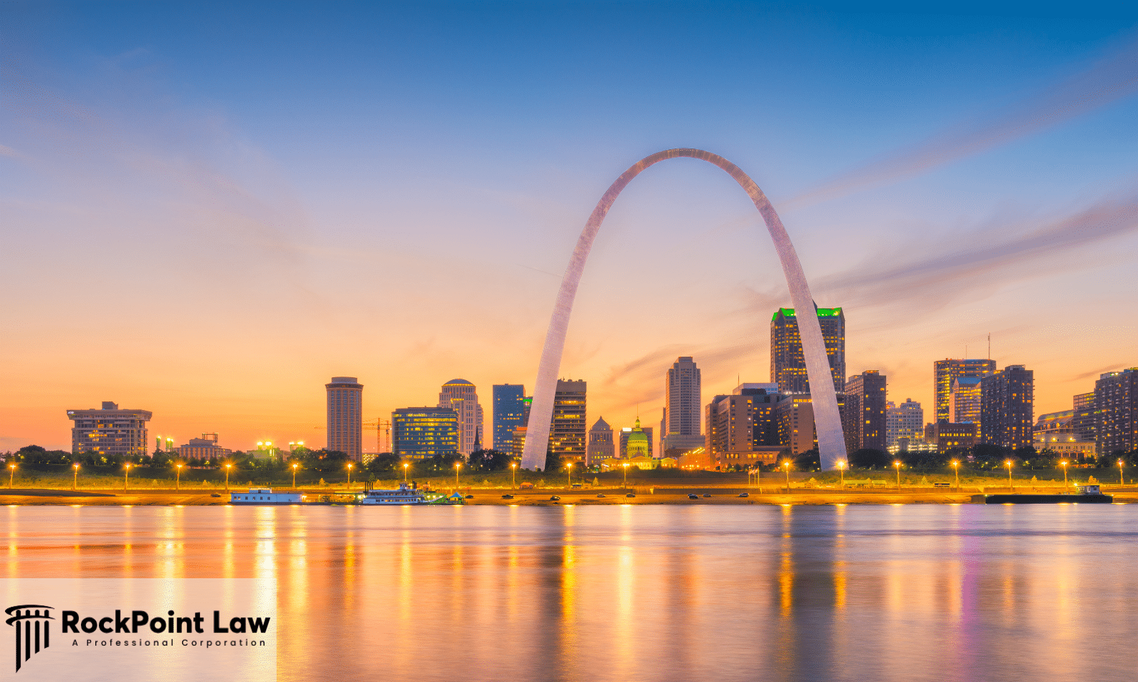 The Gateway Arch rises above the St. Louis skyline at sunset with reflections on the Mississippi River.