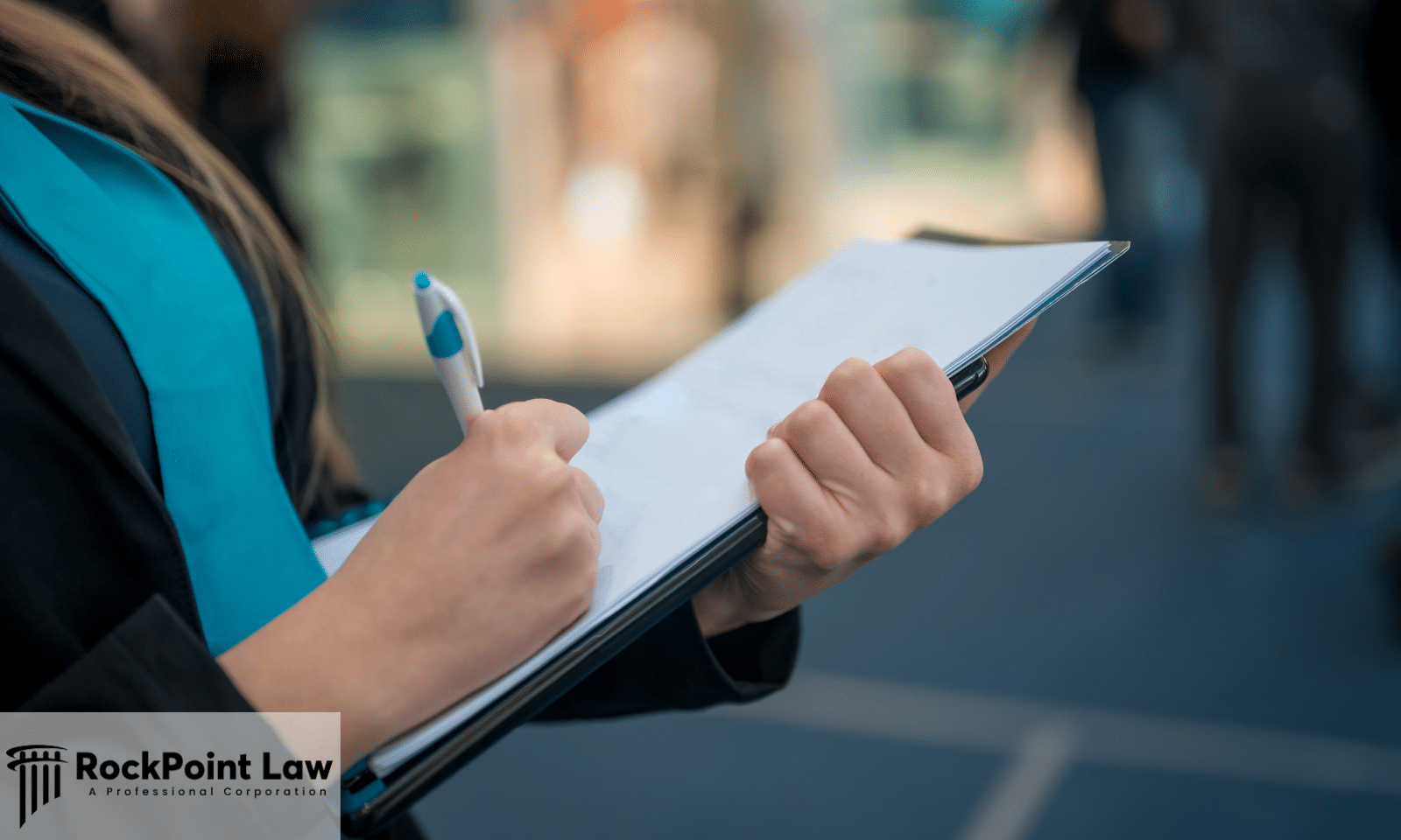 Close-up of a person writing on paperwork attached to a clipboard with a pen in a public setting.