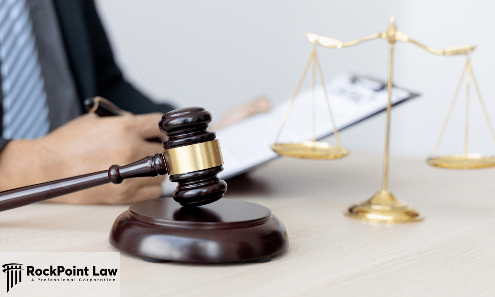 Close-up of a judge's gavel on a desk with scales of justice and an attorney reviewing legal documents.