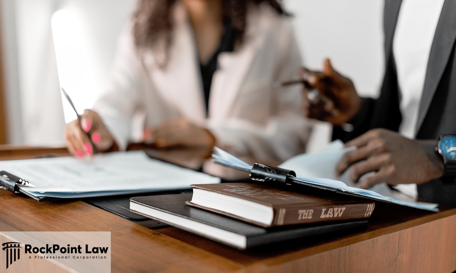 Two people reviewing paperwork across a desk beside a book titled The Law, representing a lemon law case review.