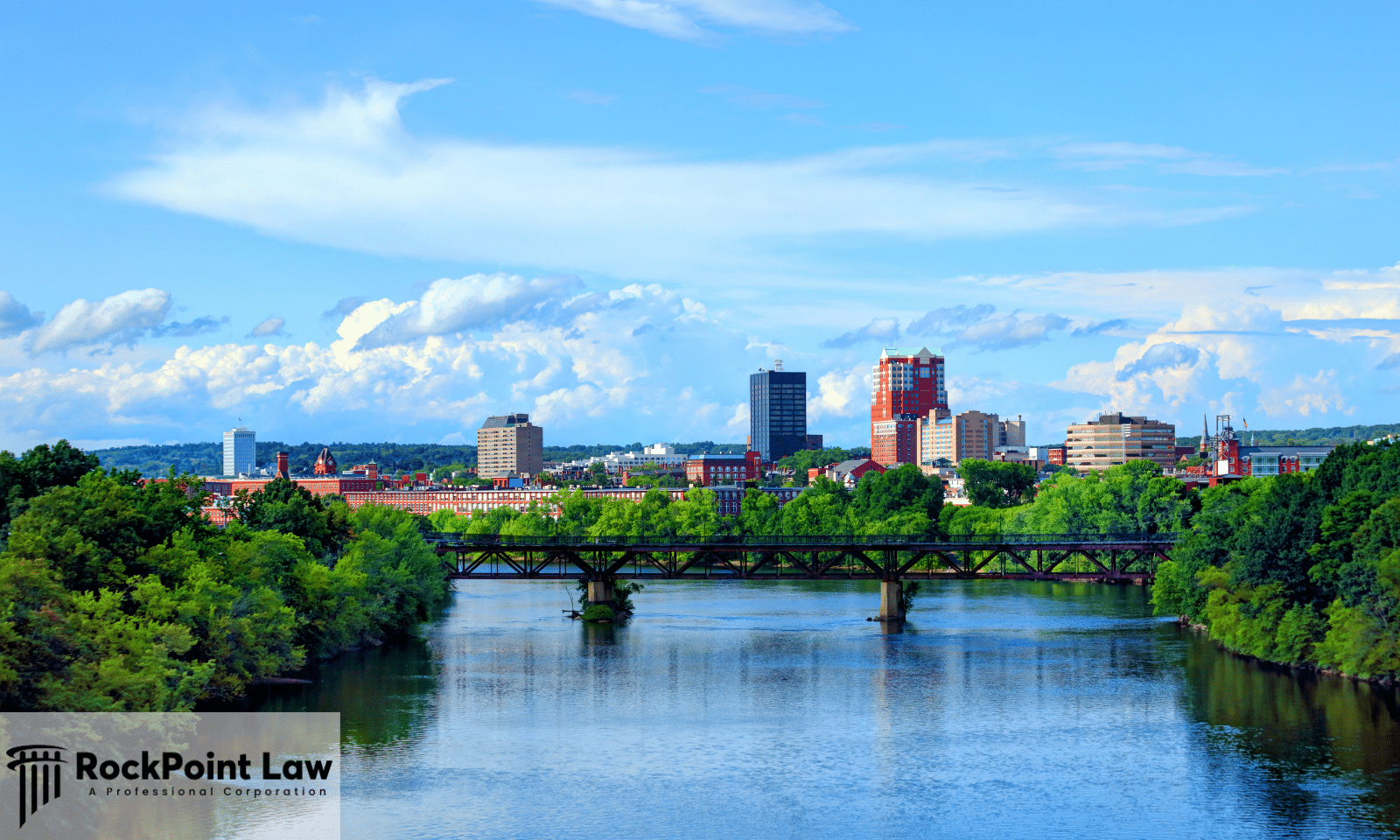 Scenic view of a New Hampshire city skyline with a bridge crossing a river, surrounded by trees.