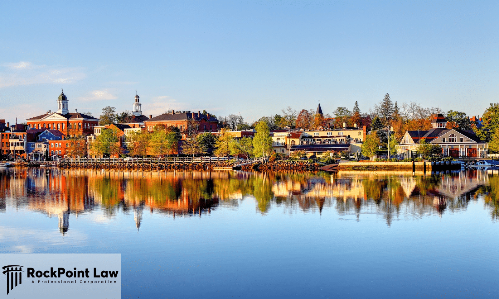 Scenic New Hampshire waterfront with historic buildings, autumn trees, and reflections on the water.