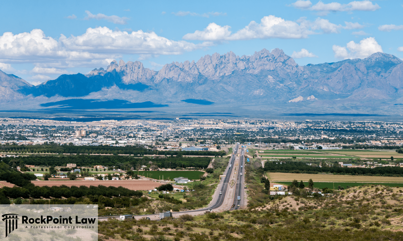 Highway leading toward a New Mexico city with mountain ranges in the background and RockPoint Law branding.