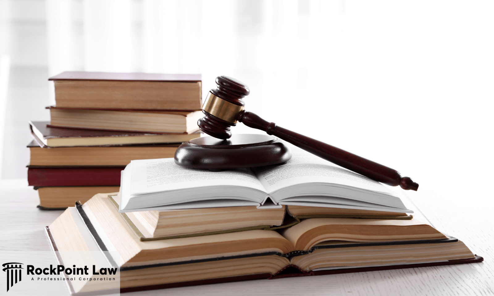 A wooden judge's gavel resting on an open law book with several stacked legal books in the background.
