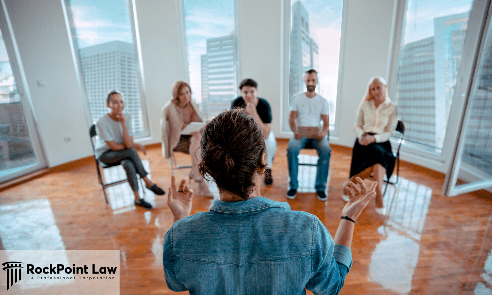 A speaker addressing a small seated group in a bright office, representing a New York lemon law arbitration hearing.