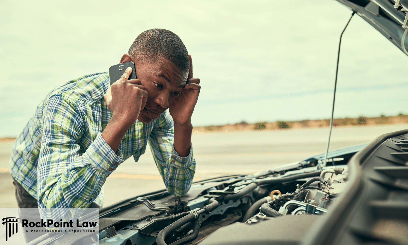 Driver on the phone looking at the engine of a broken down car at the roadside after buying it from a dealership