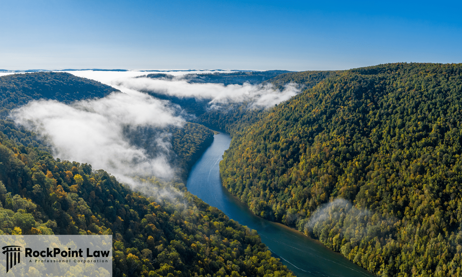 Aerial view of a forested river gorge under morning fog in West Virginia, the state whose Lemon Law protects buyers of defective new vehicles.